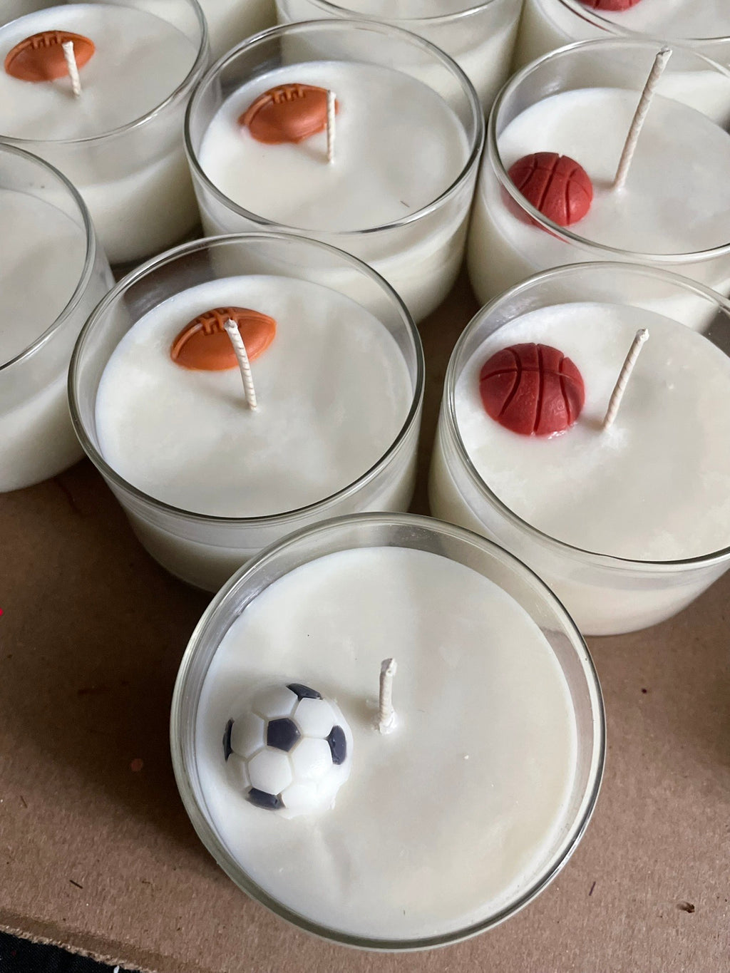 Candle holders with sports-themed wax figures on a cardboard surface