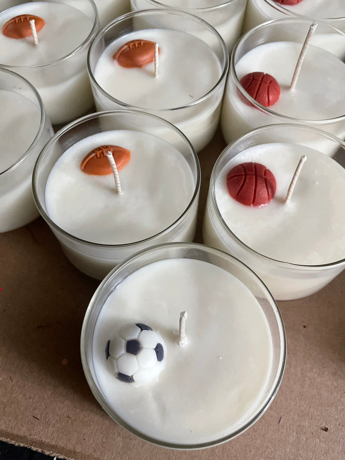 Candle holders with sports-themed wax figures on a cardboard surface